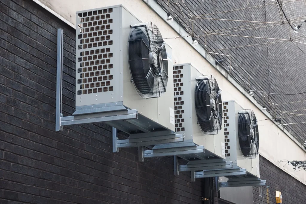 Professional ThermoSTAT Heating & Cooling    specialist inspecting outdoor condenser fans on wall brackets