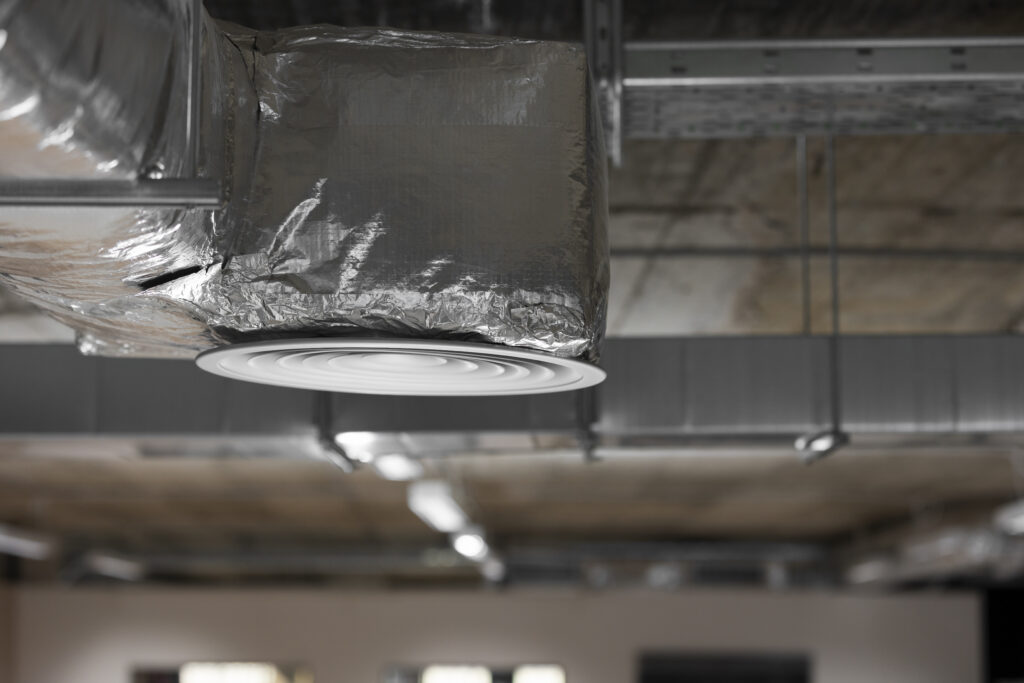 Exposed insulated HVAC duct leading to circular ceiling diffuser in commercial space